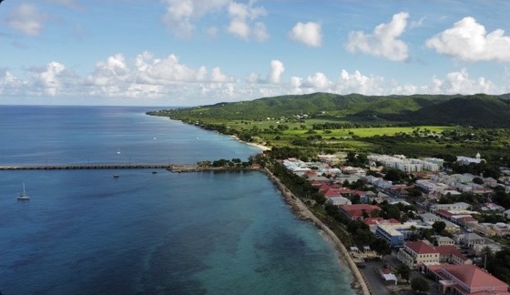 Aerial view of a Caribbean harbor town, coastline, and green hills
