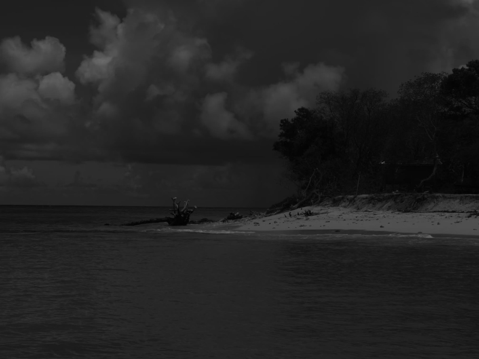 A lone boat resting on a quiet Caribbean shoreline under dramatic skies